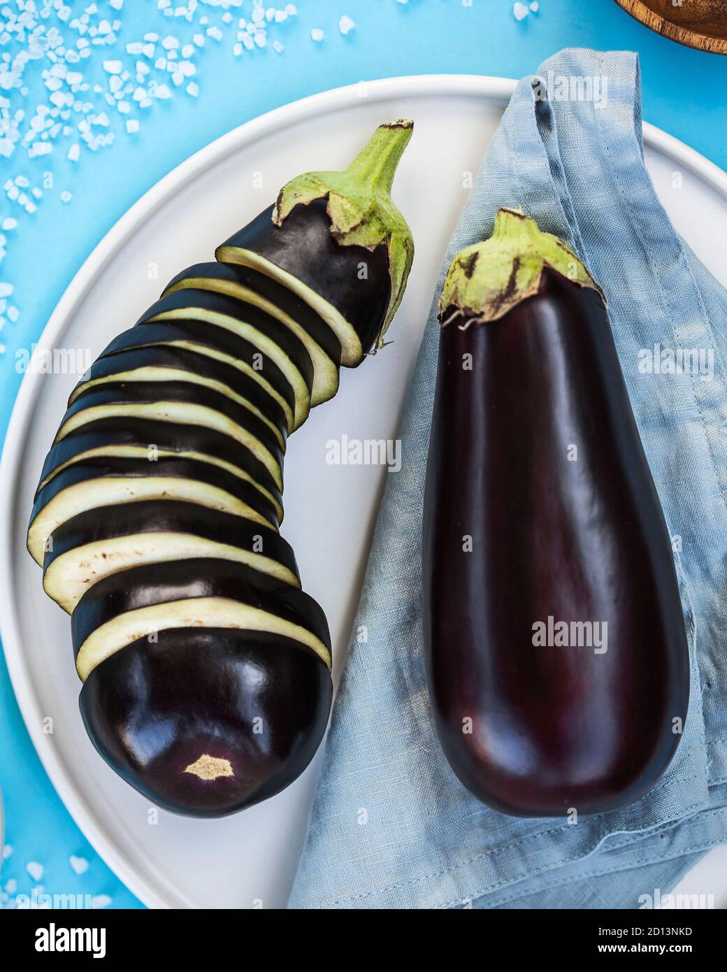 Reife Bio Aubergine ganz und in Scheiben geschnitten auf einem weißen Teller auf einem blauen Hintergrund. Food Foto für ecomarket. Stockfoto