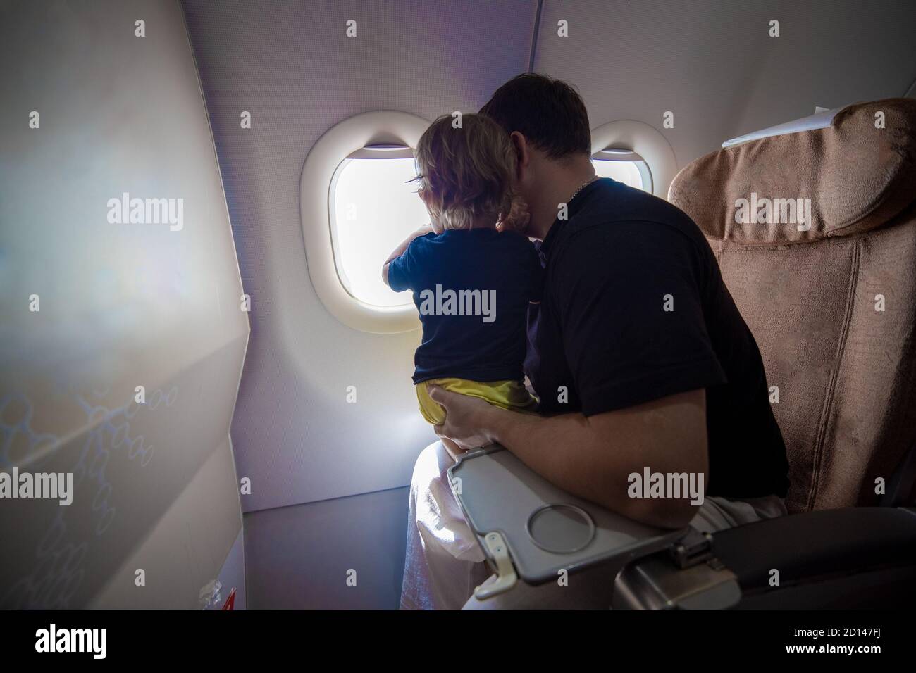 Vater und niedliche Kleinkind sitzen auf einem Flugzeug und Blick in den Himmel durch das Bullauge. First Flight Konzept, Reisen mit Kindern Stockfoto