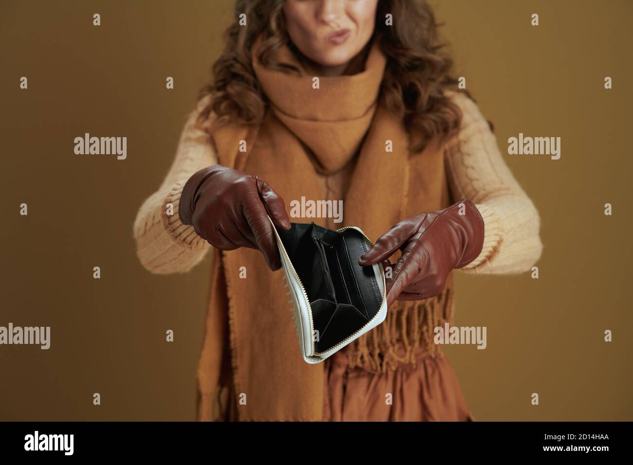 Hallo september. Nahaufnahme einer unglücklichen Frau mittleren Alters im Schal mit Geldbörse und Lederhandschuhen vor bronzefarbenem Hintergrund. Stockfoto