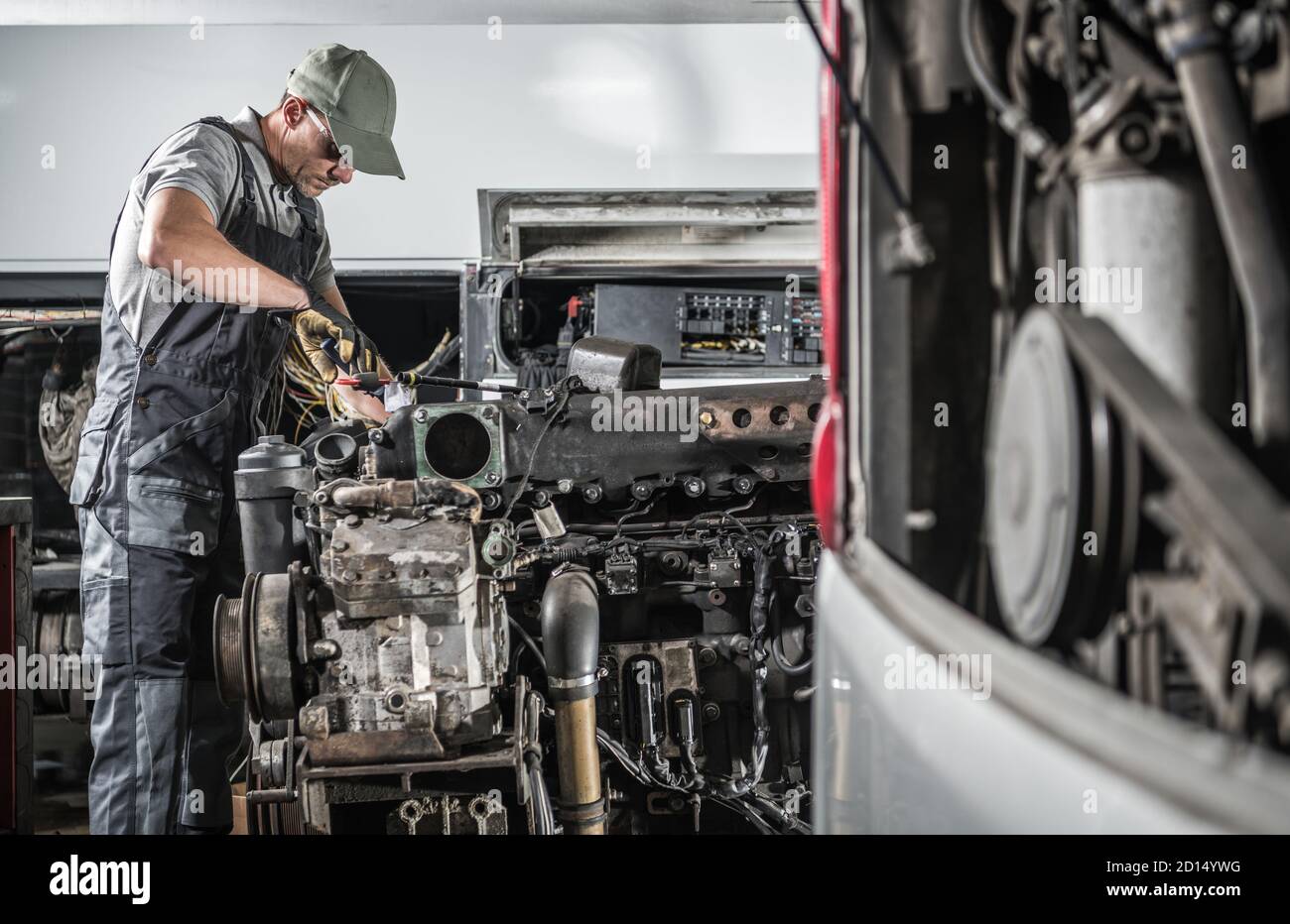 Professioneller Kaukasischer Kfz-Mechaniker in seinen 40er Jahren, der leistungsstarke Hochleistungs-Lkw- oder Bus-Dieselmotoren im Truck Service Center repariert. Transporta Stockfoto