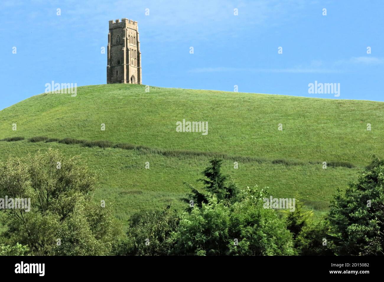 St. Michael's Tower erhebt sich über grünem Gras und Bäumen am Glastonbury Tor, einem Hügel in England, der mit König Arthur verbunden ist Stockfoto