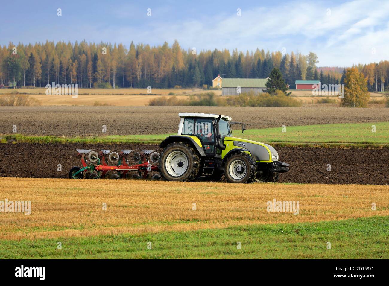 Bauer pflügt Feld mit grünen Valtra Traktor und Pflügen an einem sonnigen Herbstmorgen in Südfinnland. Jokioinen, Finnland. Oktober 2020 Stockfoto