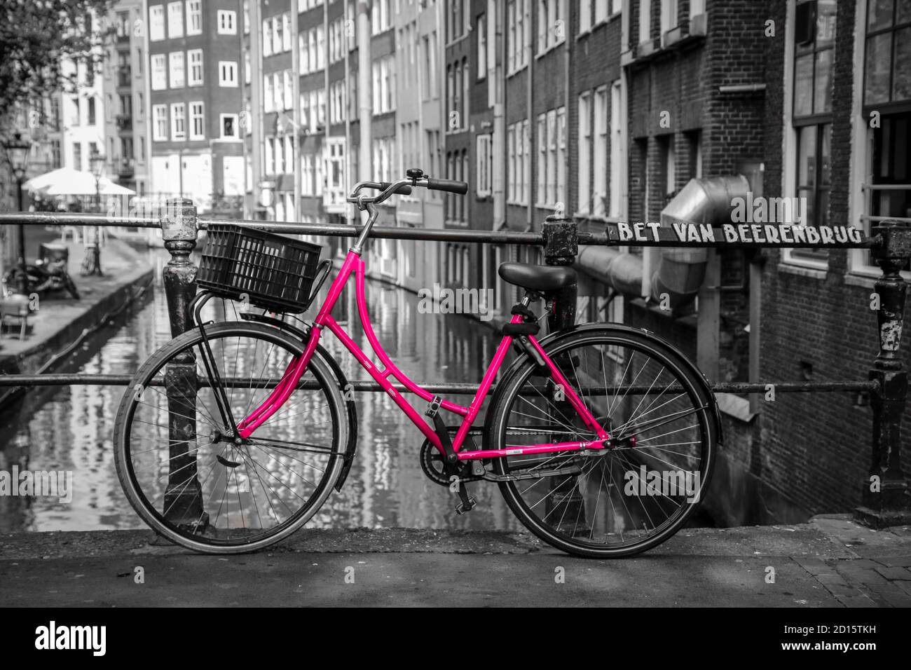 Ein Bild von einem rosa Fahrrad auf der Brücke über den Kanal in Amsterdam. Der Hintergrund ist schwarz-weiß. Stockfoto