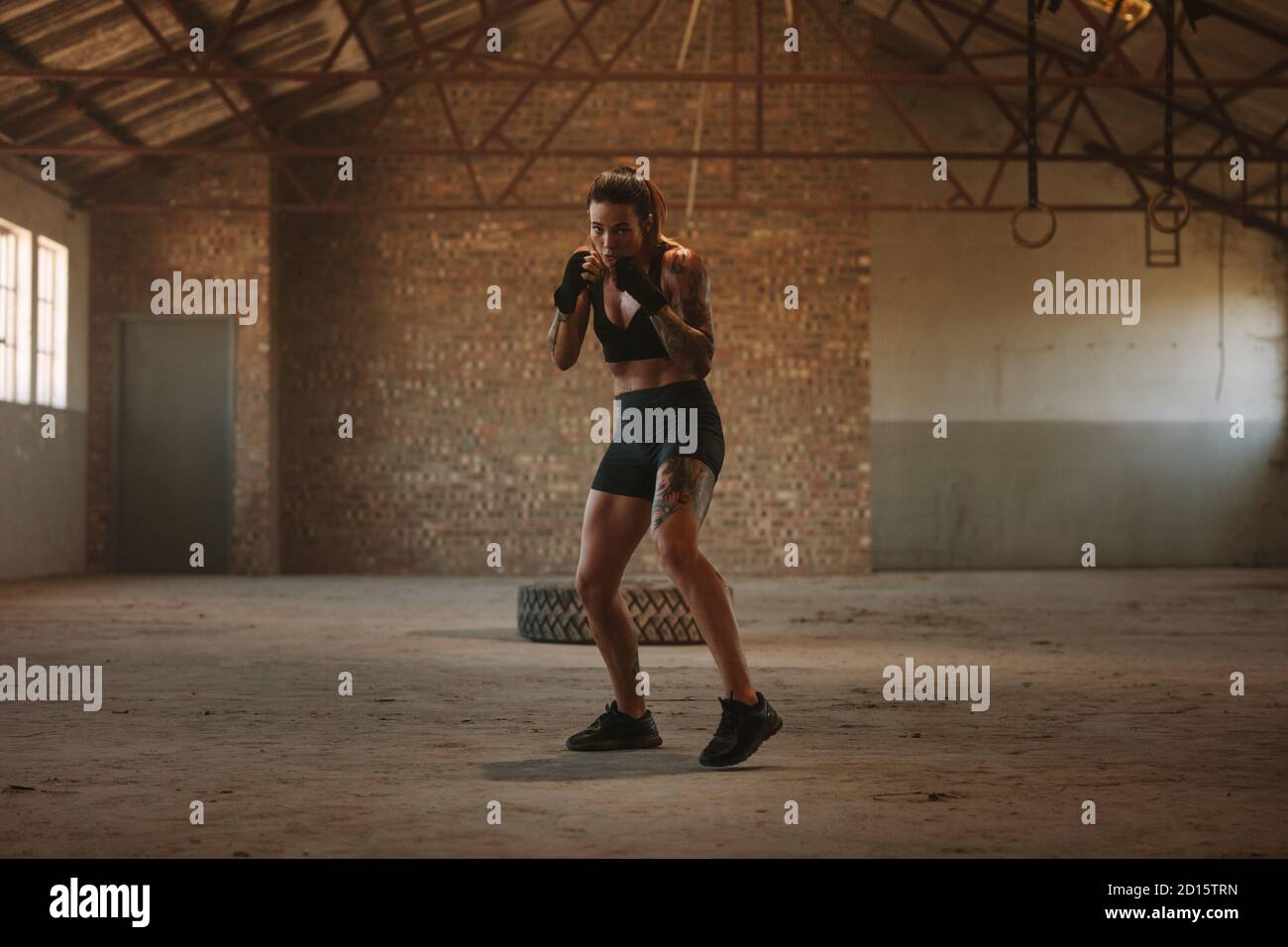 Frau tut Schattenboxen Übung in leeren Fabrik Schatten. Frau in Sportkleidung übt ihre Schläge in einem verlassenen Lager. Stockfoto