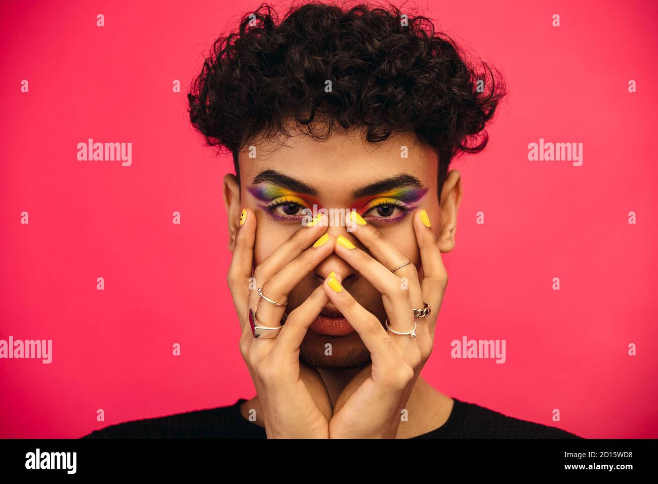 Geschlecht Flüssigkeit männlich trägt regenbogenfarbenen Lidschatten und Smiley Gesicht auf Fingernagel. Transgender männlich mit funky Make-up auf rotem Hintergrund. Stockfoto
