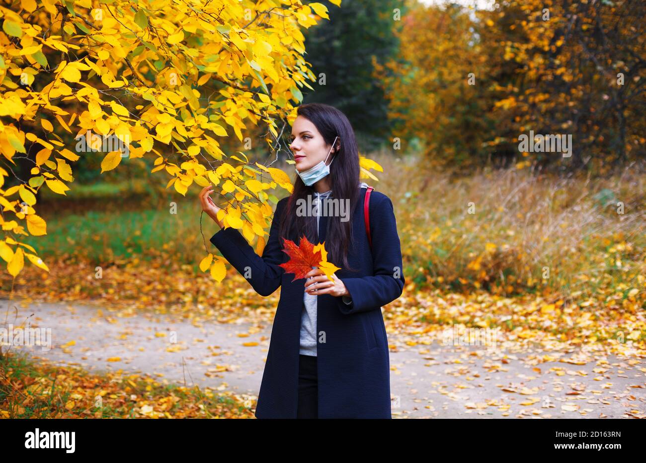 Frau mit abgesenkter Schutzmaske geht im Herbstpark. Zeit in der Natur während des Coronavirus-Ausbruchs. Stockfoto