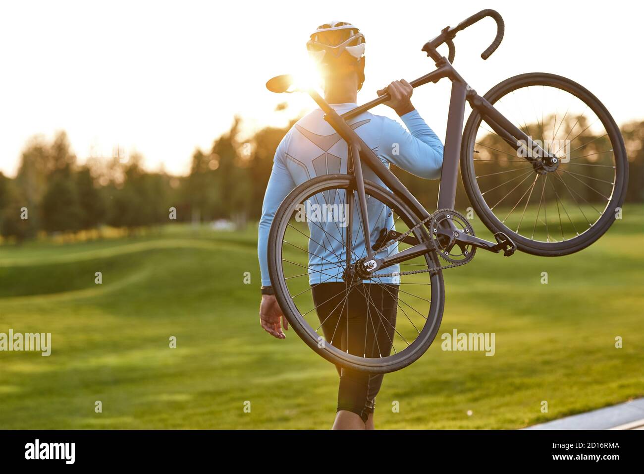 Starker sportlicher Mann in Sportkleidung, der sein Fahrrad trägt und nach dem Radfahren im Park den atemberaubenden Sonnenuntergang beobachtet. Aktiver Lebensstil und Sport. Radfahren im Freien Stockfoto