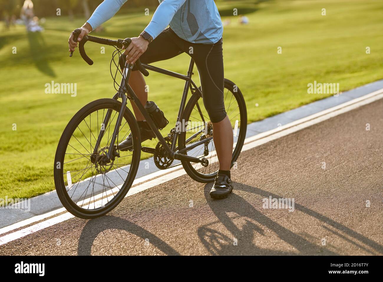 Radfahren bei Sonnenuntergang. Ein kurzer Schuss eines Mannes in Sportkleidung, der an einem Sommertag mit seinem Fahrrad auf der Straße im Park steht. Aktiver Lebensstil und Sport Stockfoto