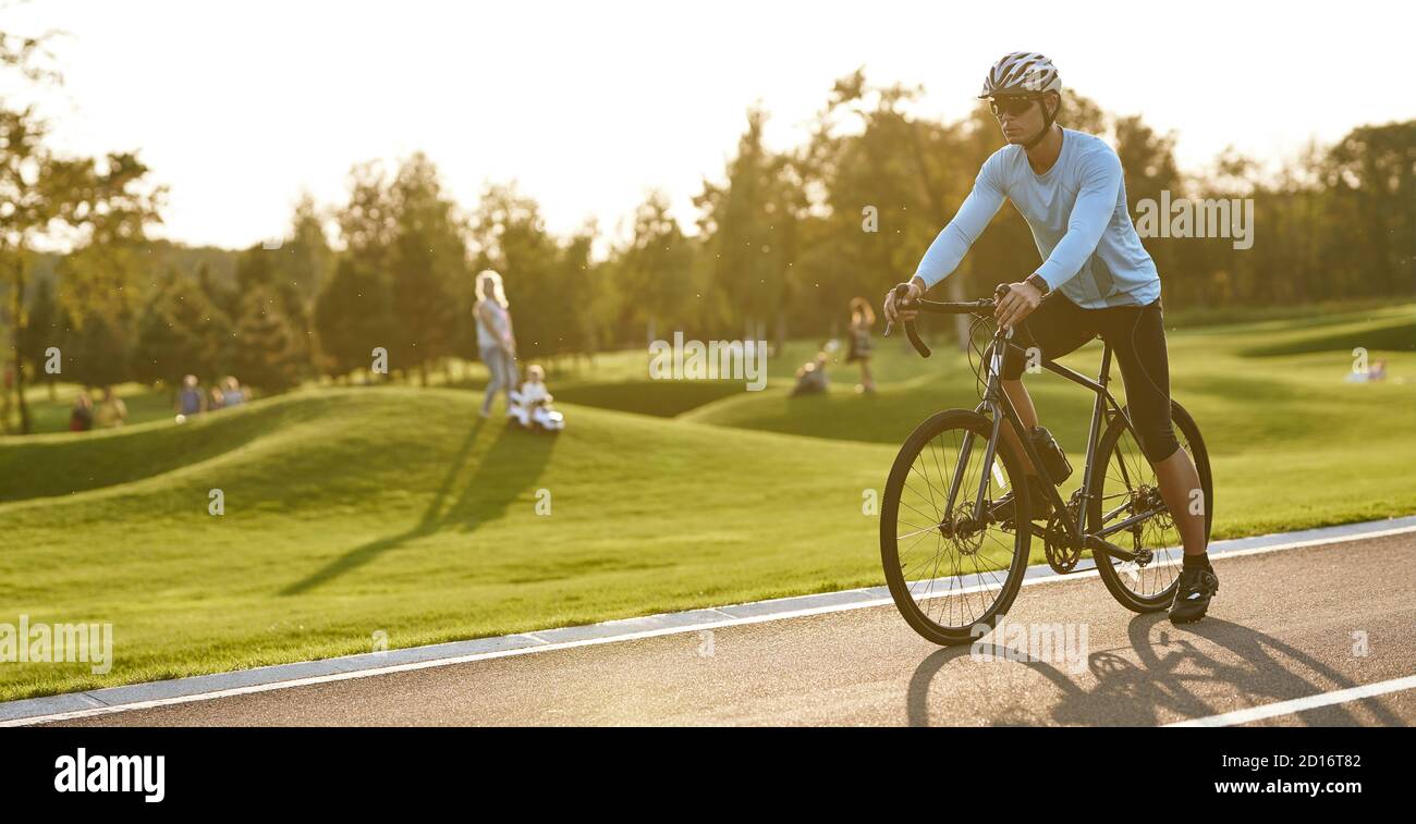 Professionelle Rennrad Racer Training im Freien. Junger Sportler in Sportbekleidung und Schutzhelm stehen mit Fahrrad auf der Straße im Park, immer bereit zu fahren. Aktiver Lebensstil und Sport Stockfoto