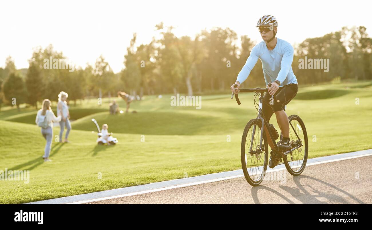 Aktiver Lebensstil. Junger Sportler in Sportbekleidung und Schutzhelm Reiten Mountainbike im Park während Sonnenuntergang, Radfahren im Freien an einem Sommertag Stockfoto