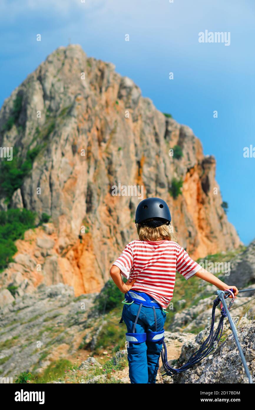 Kind in Sicherheitsausrüstung Untergestell oben. Sehen Sie sich die atemberaubende Landschaft an. Familienreise, Klettersteig-Abenteuer, Wanderaktivitäten. Kinder erkunden die Natur Stockfoto