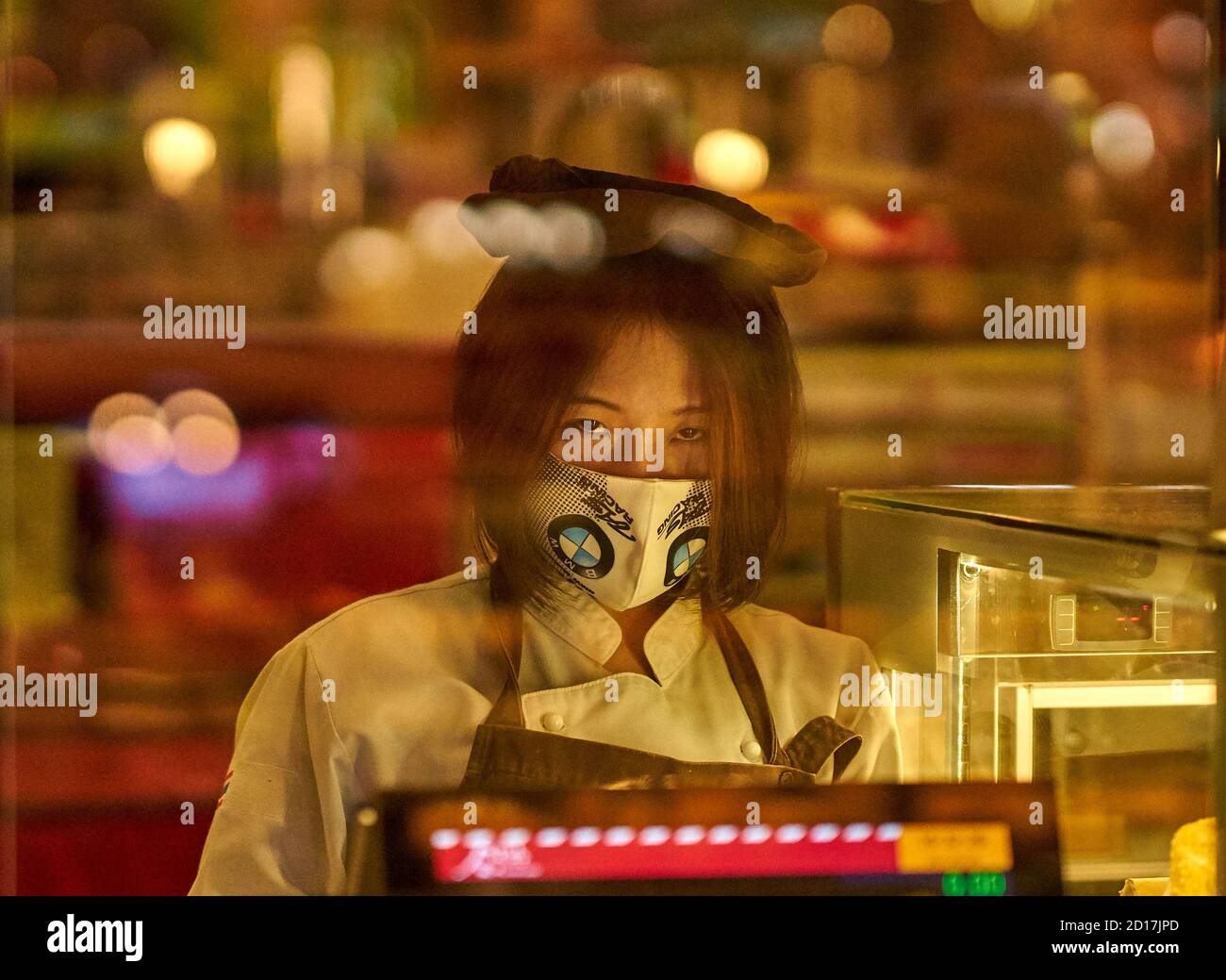 Eine Verkäuferin in einem Lebensmittelgericht, die eine schützende Gesichtsmaske trägt. Stockfoto