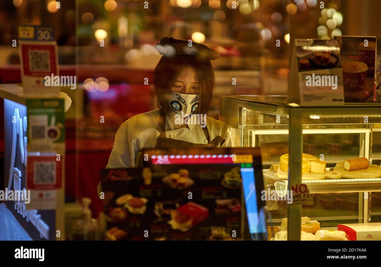Eine Verkäuferin in einem Lebensmittelgericht, die eine schützende Gesichtsmaske trägt. Stockfoto