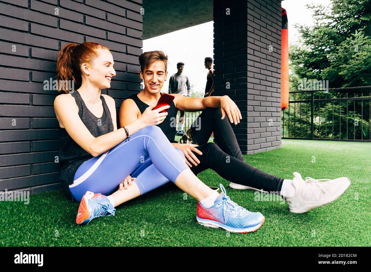 Eine junge Frau spricht mit einem jungen Mann und zeigt Er ihr Smartphone nach dem Training im Fitnessstudio Stockfoto