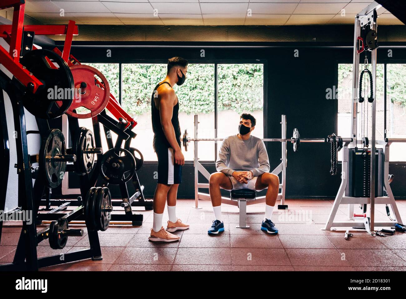 Zwei Männer mit Gesichtsmasken sprechen beim Arbeiten an Der Fitnessraum Stockfoto