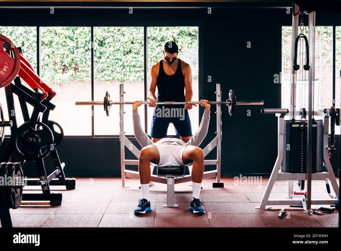 Personal Trainer trägt eine Gesichtsmaske hilft jungen Männern durchführen Ihre Übungen im Fitnessstudio Stockfoto