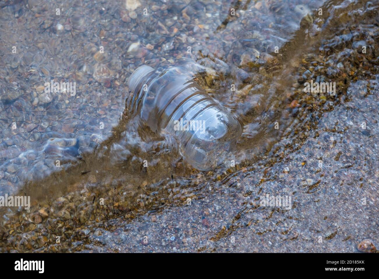 Eine weggeworfene Plastikflasche Müll weggeworfen auf Das Ufer fing in der Strömung auf dem felsigen Strand Die Umwelt verschmutzen Stockfoto