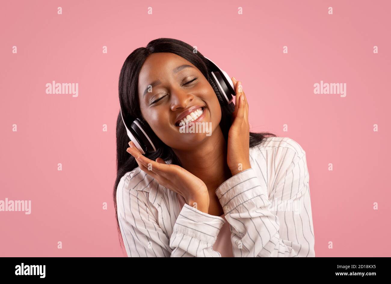 Porträt einer hübschen afroamerikanischen Frau, die Kopfhörer trägt und hört Zu schöner Musik auf rosa Studio Hintergrund Stockfoto