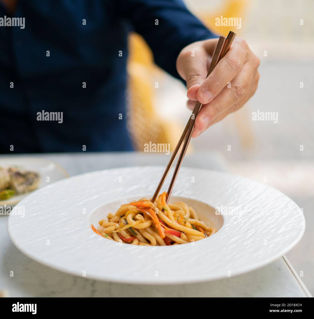 Mann essen asiatische vegetarische Lebensmittel udon Nudeln mit Baby bok Choy, Shiitake Pilze, Sesam und Pfeffer Nahaufnahme auf einem weißen Teller auf dem Tisch. Front vie Stockfoto
