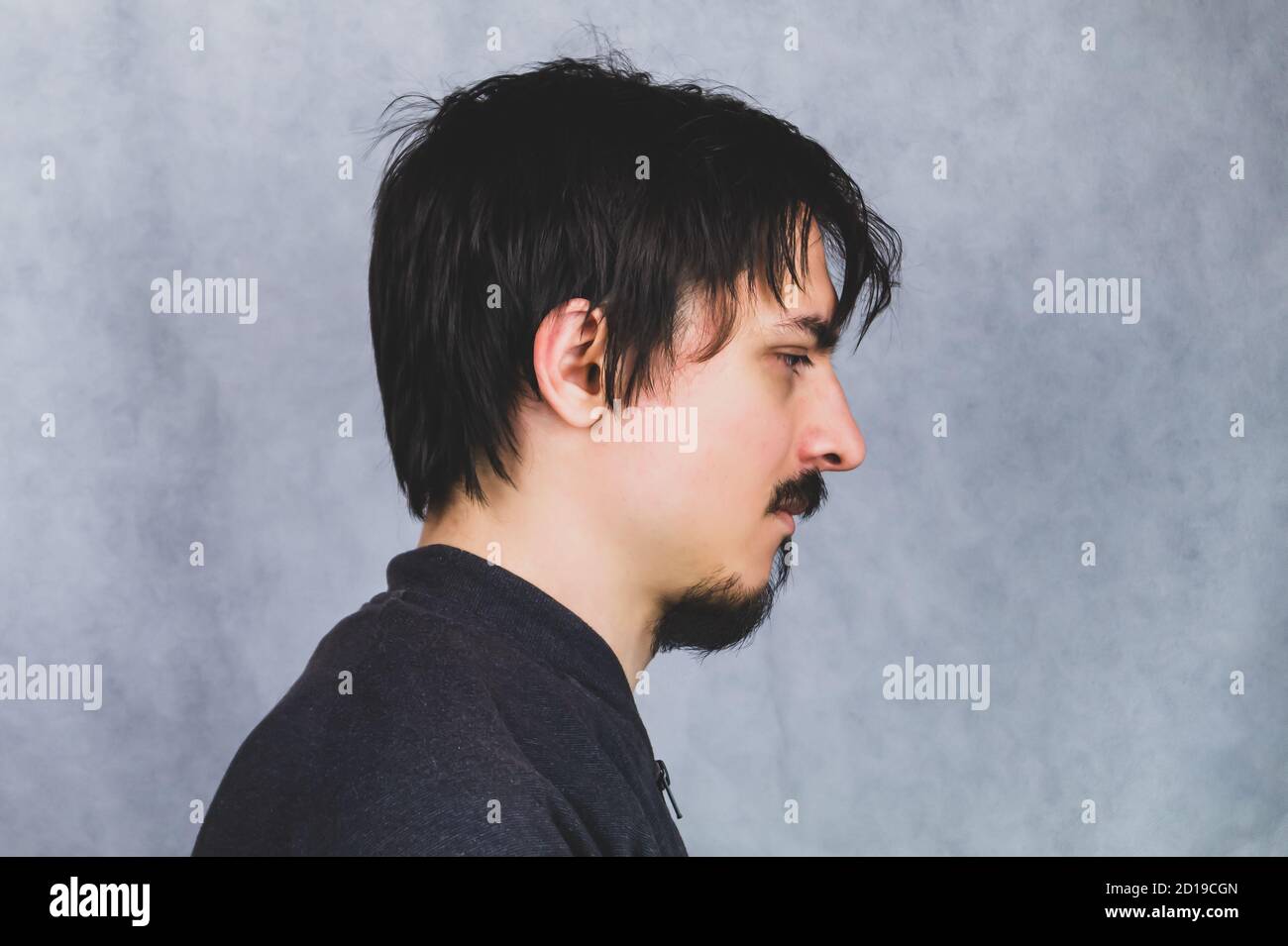 Profilansicht des jungen Mannes mit schwarzen Haaren auf dem Grauer Hintergrund Stockfoto