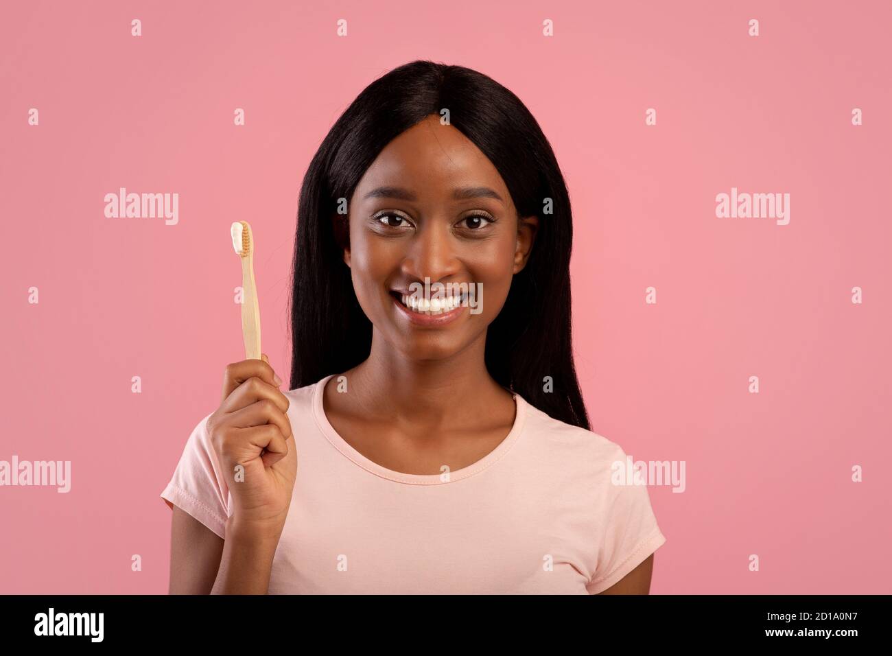 Portrait der schönen afroamerikanischen Frau mit strahlendem Lächeln halten Zahnbürste aus Holz mit Paste auf rosa Hintergrund Stockfoto