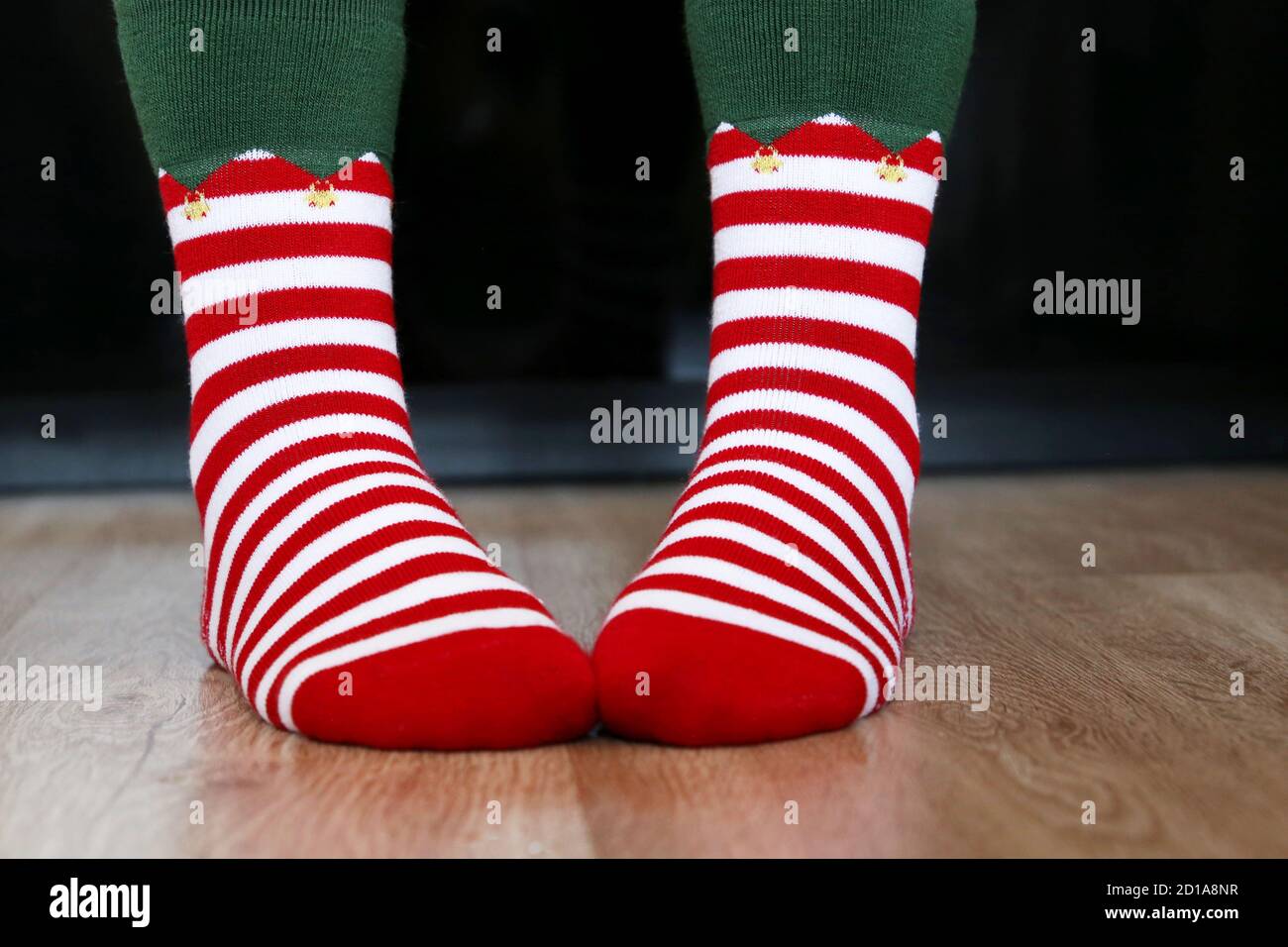 Weibliche Füße in Weihnachtssocken auf dem Holzboden. Konzept der Neujahrsfeier, Elf Kostüm Stockfoto
