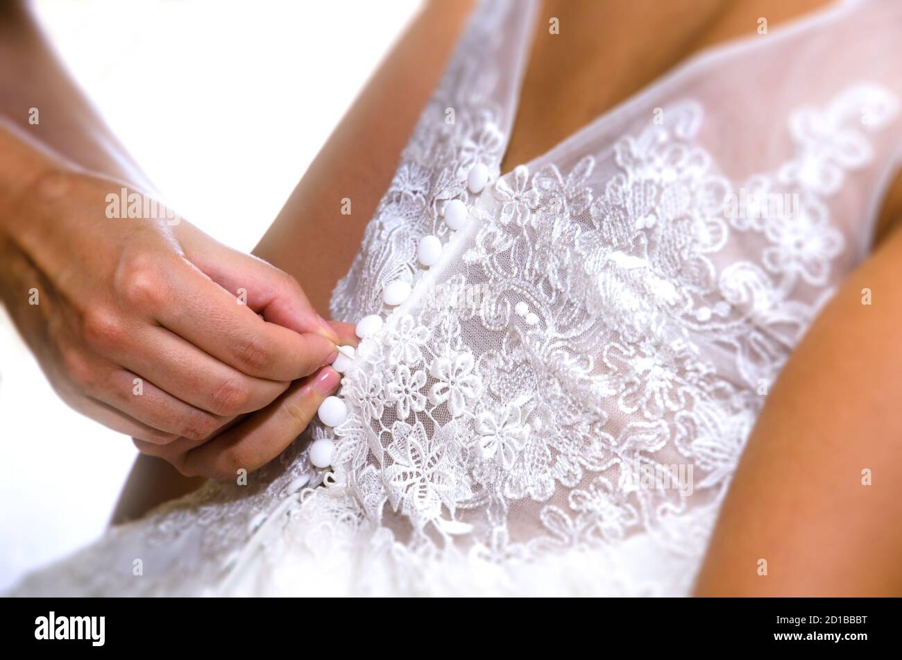 Mamas Hände schließen das Hochzeitskleid der Braut Stockfoto