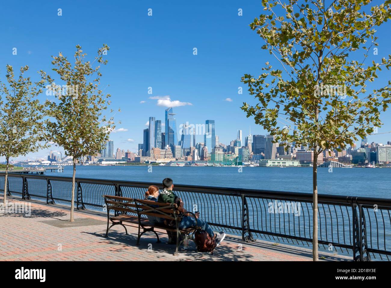 Pärchen sitzen auf der Bank und genießen den Blick auf die Skyline von New York City/Manhattan von der anderen Seite des Hudson River in Hoboken, New Jersey's Waterfront. Stockfoto
