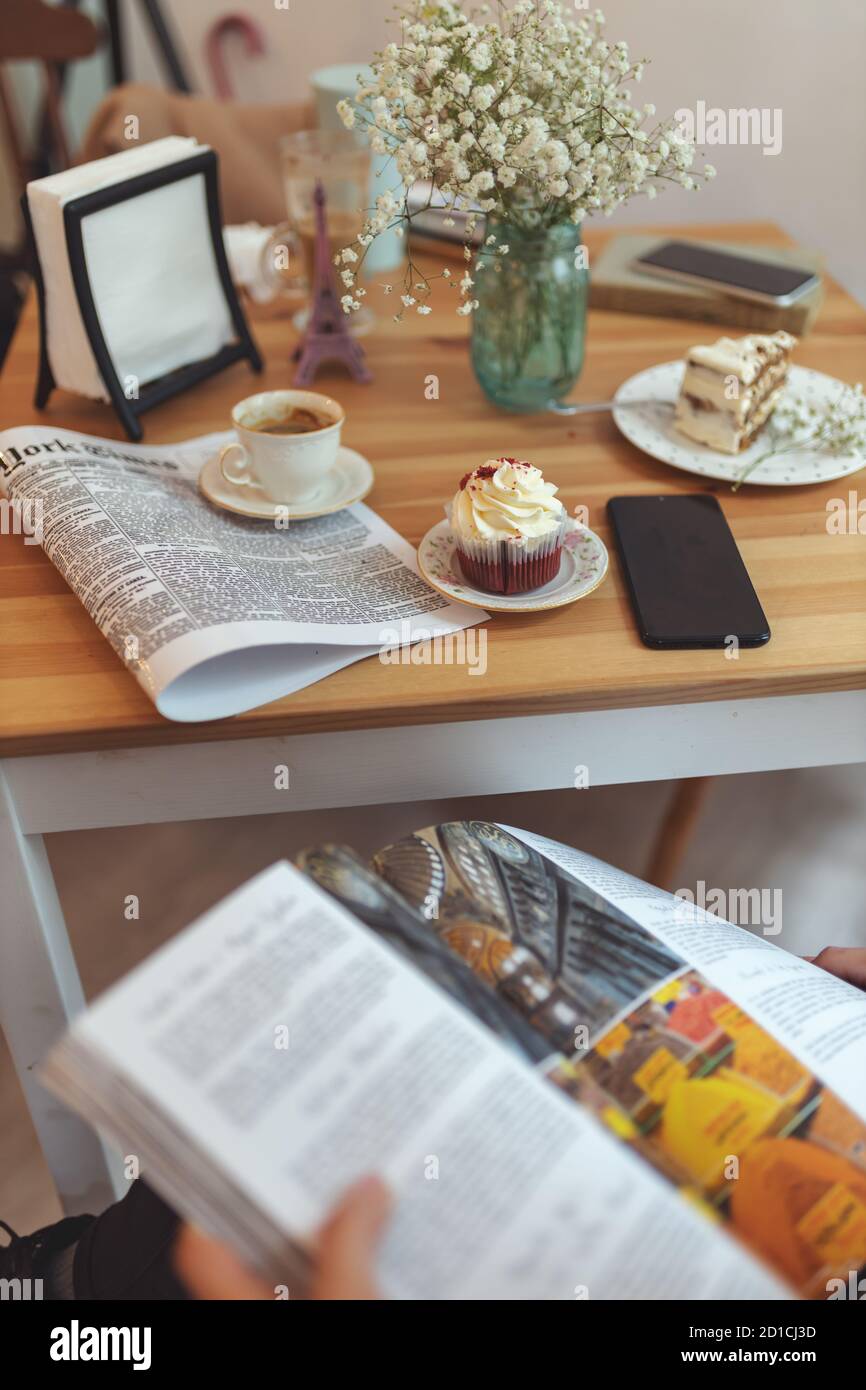 Mädchen liest ein Magazin vor einem Tisch mit Eine Tasse Kaffee und Desserts darauf Stockfoto