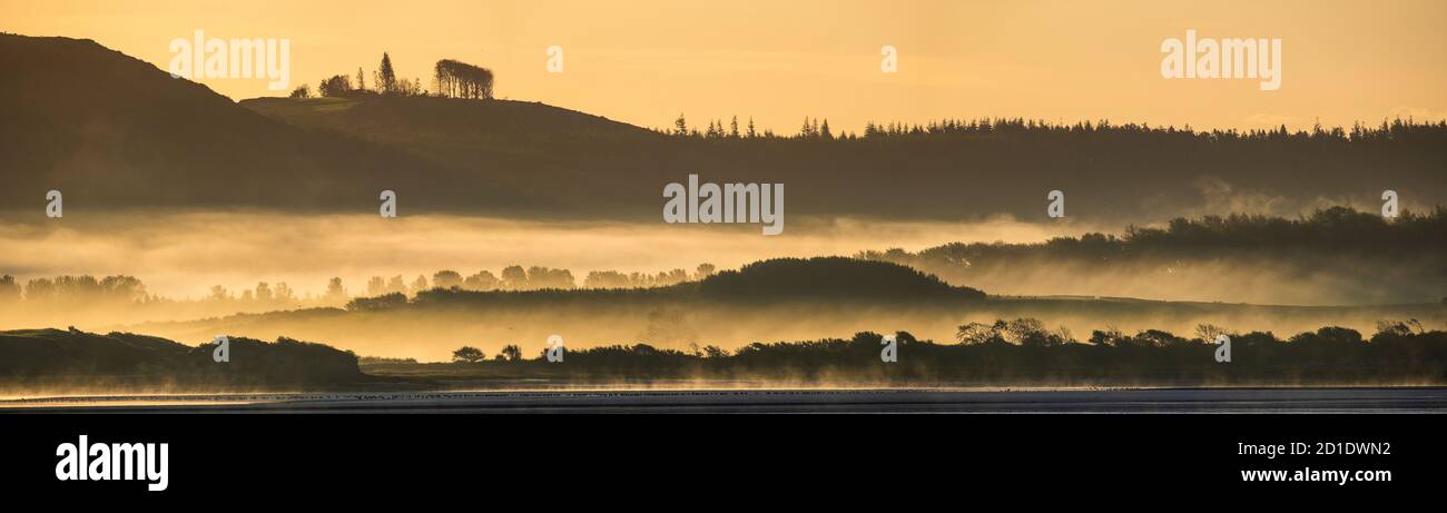 Am frühen Morgen hängt Nebel um den Fuß der Cartmel Fells und Ronudsea Wood auf der anderen Seite der Leven Mündung. Stockfoto