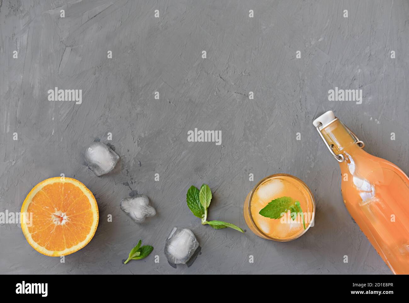 Orangen- und Orangensaft in einer Flasche und in einem hohen Glas. Minzblätter auf grauem Hintergrund. Eiswürfel schmelzen. Sommerfrische saftige Früchte. Kalte Sommergetränke. Stockfoto