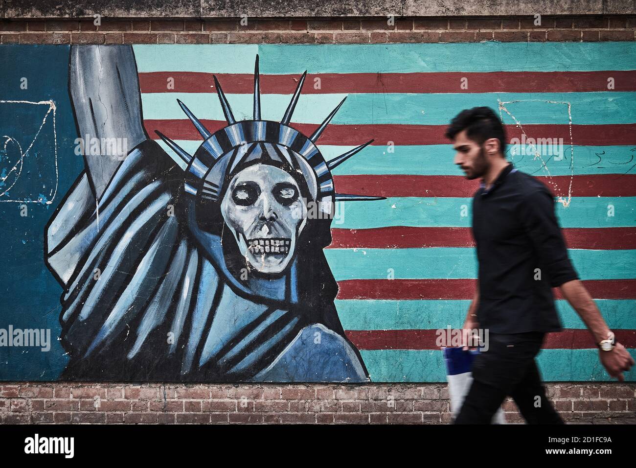 Mann geht vor eine Wand der alten Botschaft Der Vereinigten Staaten mit einem Graffiti mit der Flagge der USA Mit der Freiheitsstatue mit einem Totenkopf Stockfoto