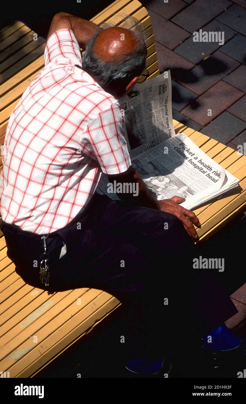 Mann sitzt auf einer Sitzbank und liest Zeitung, Perth, Westaustralien Stockfoto