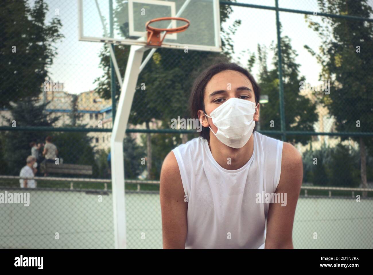 Langhaarige Teenager trägt eine Schutzmaske vor ruhen Des Basketballkorbs Stockfoto