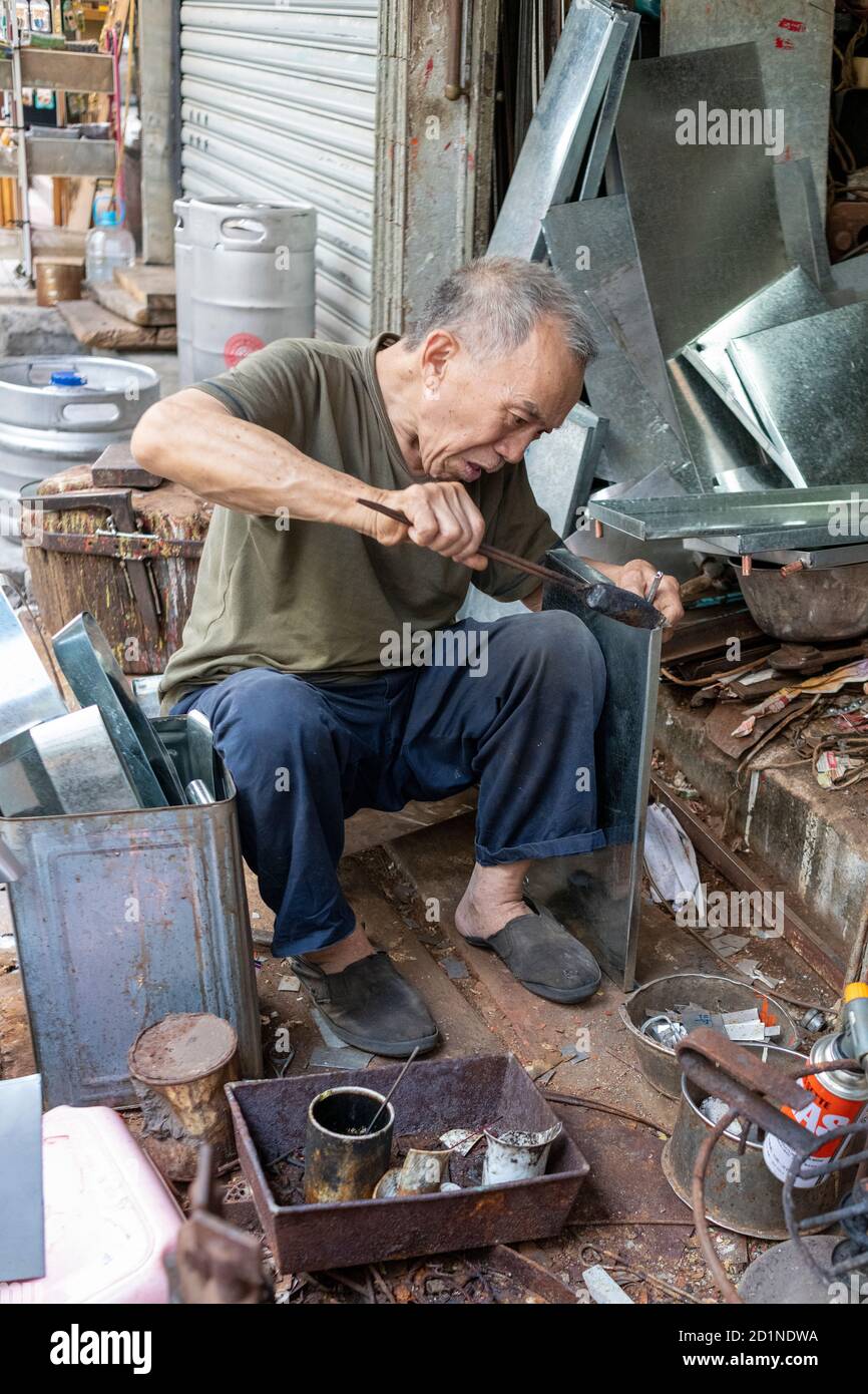 Mann, der Reparaturen an verschiedenen Metallgegenständen auf dem Fußweg durchführt. Stockfoto