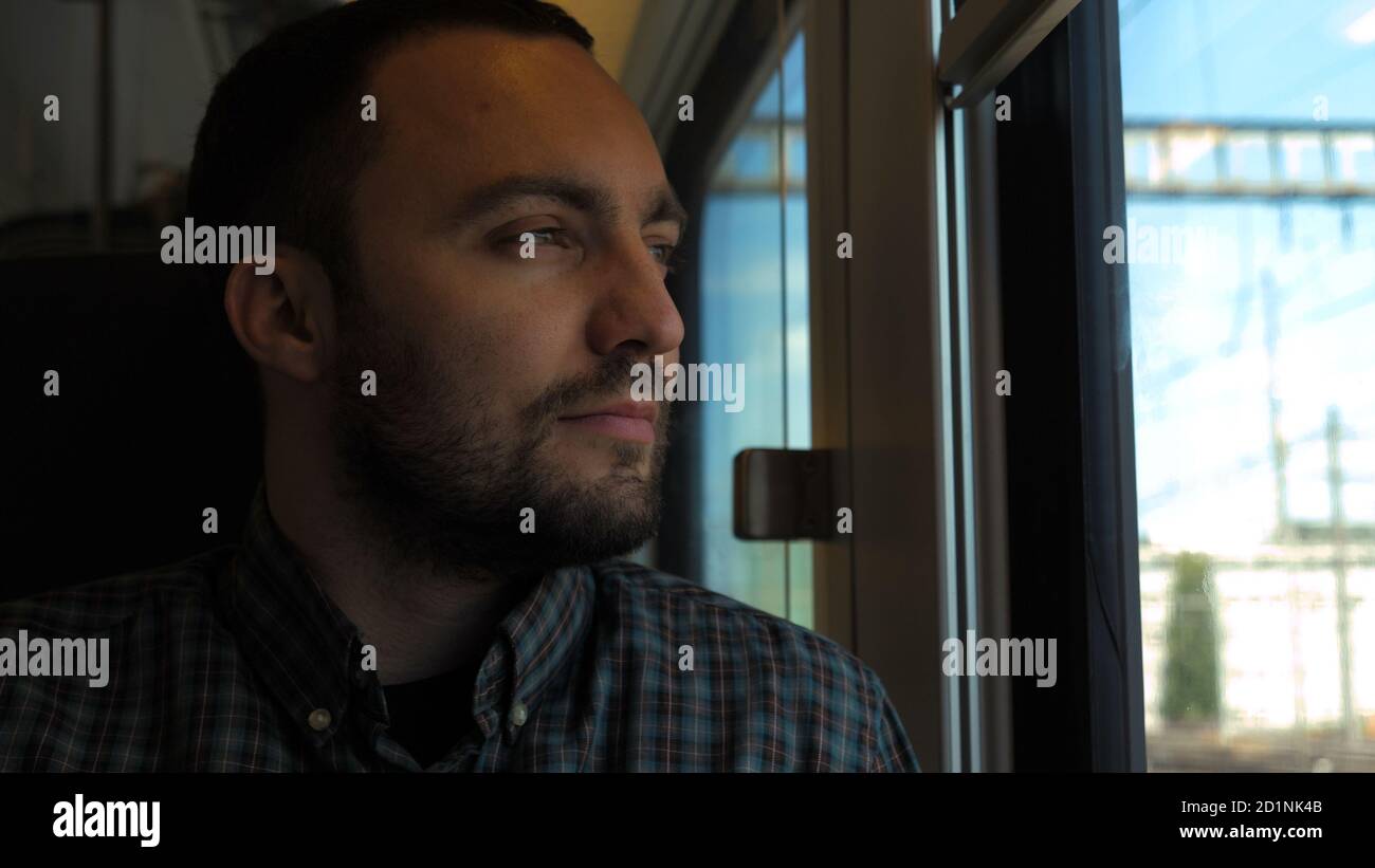 Ein fröhlicher junger Mann, der in einem Zug am Fenster sitzt. Stockfoto