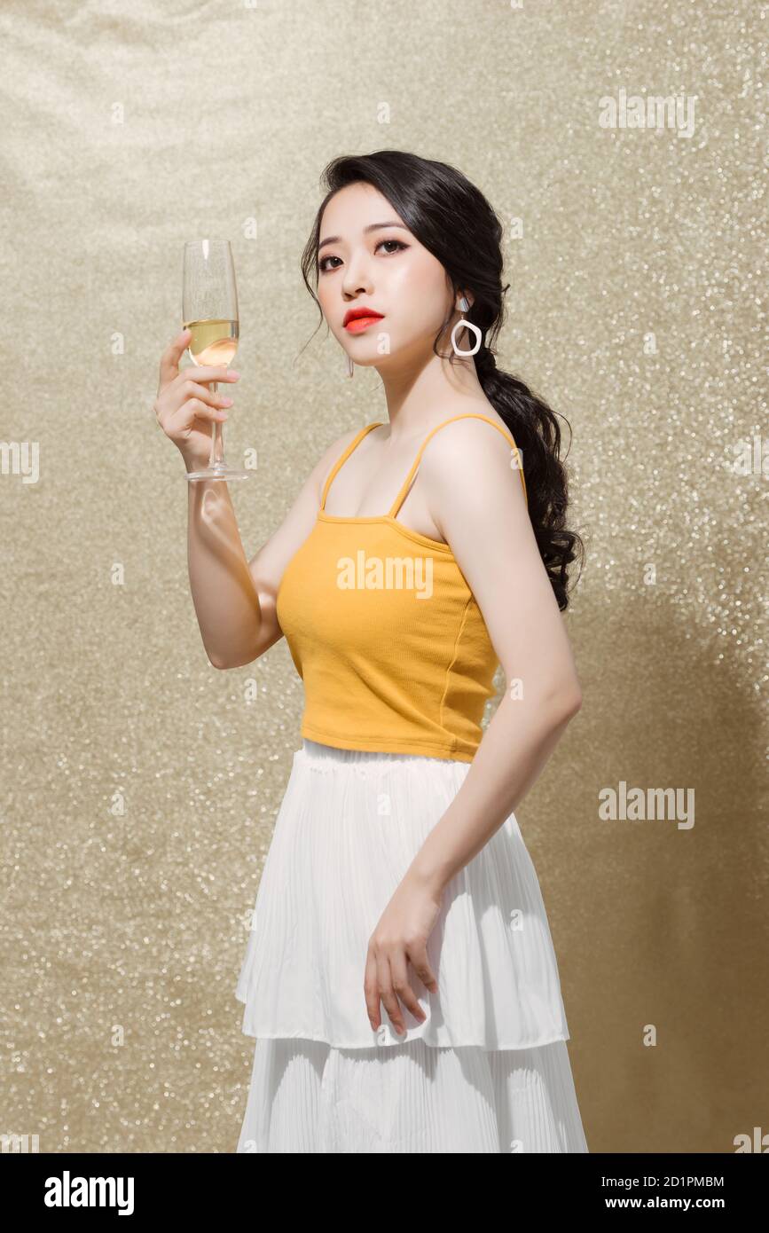 Innenaufnahme der positiven attraktiven jungen Frau in Abendkleid mit einem Glas Champagner, Stockfoto