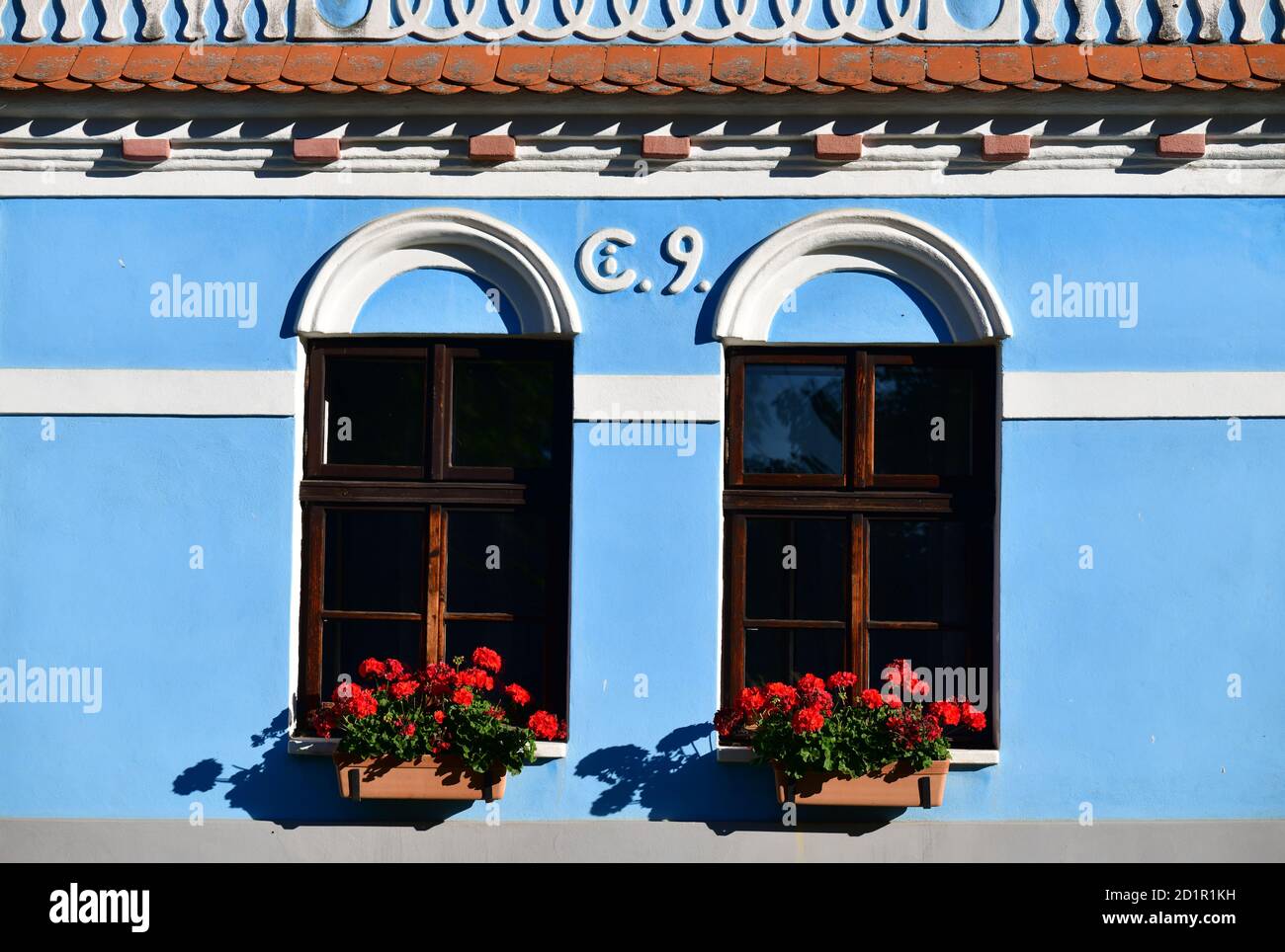 Fassade des blauen traditionellen tschechischen Landhauses. Fenster, dekoriert mit roten Blumen. Böhmen, Tschechische Republik Stockfoto