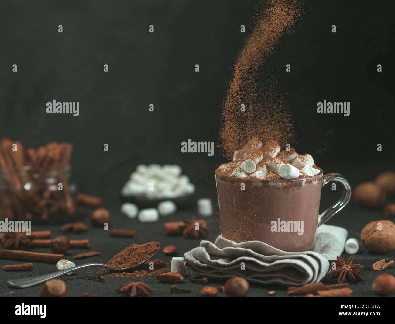 Hand bestreut Zimtpulver auf Glas Becher mit heißer Schokolade Kakao trinken. Kopieren Sie Platz. Der dunkle Hintergrund. Low Key. Winter Essen und Trinken Konzept. Stockfoto
