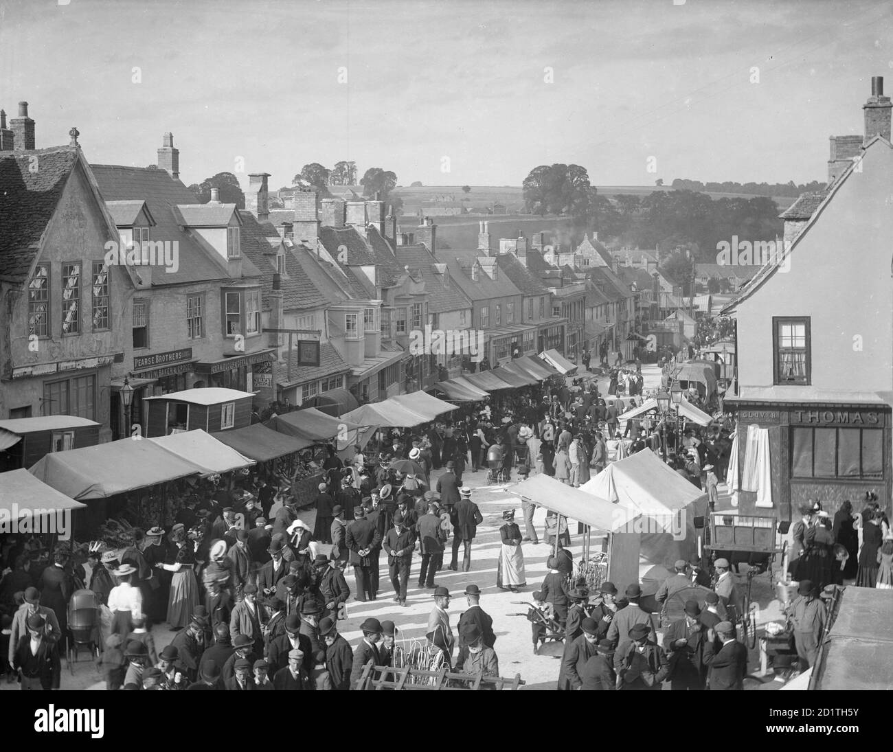High Street, Burford, Oxfordshire. Ein Blick auf die Straße während der Verleihmesse (Mop Fair) mit Ständen eingerichtet. Stockfoto