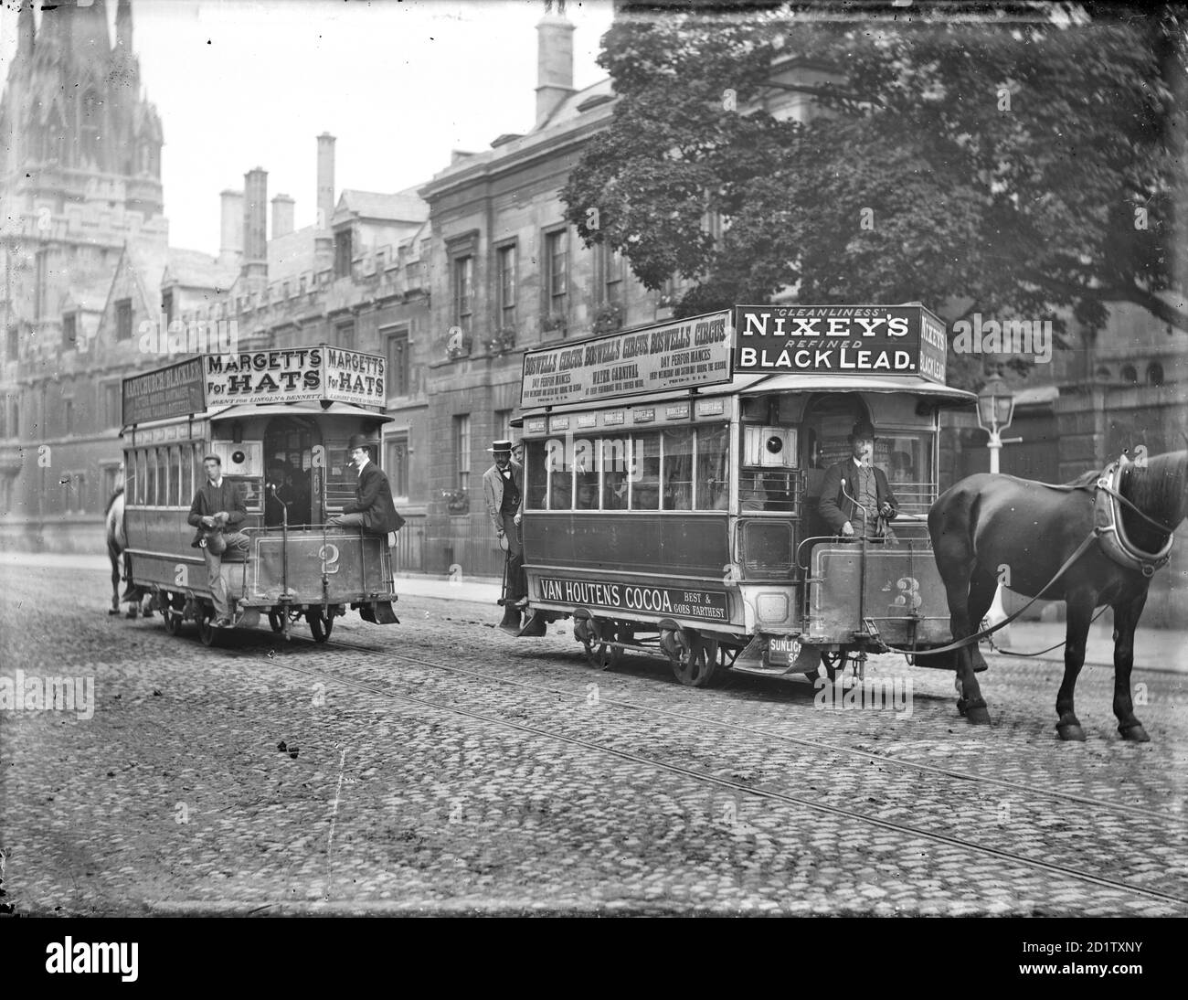 High Street, Oxford, Oxfordshire. Zwei Pferdebahnen, die in der Straße vorbeifahren, mit Werbetafeln, die an den Dächern angebracht sind. Magdalen Bridge wurde im Jahr 1899 von der Oxford Local Board erweitert, um Platz für Pferdestraßenbahnen, aber von 1913 Autobusse hatten ihren Auftritt. Stockfoto