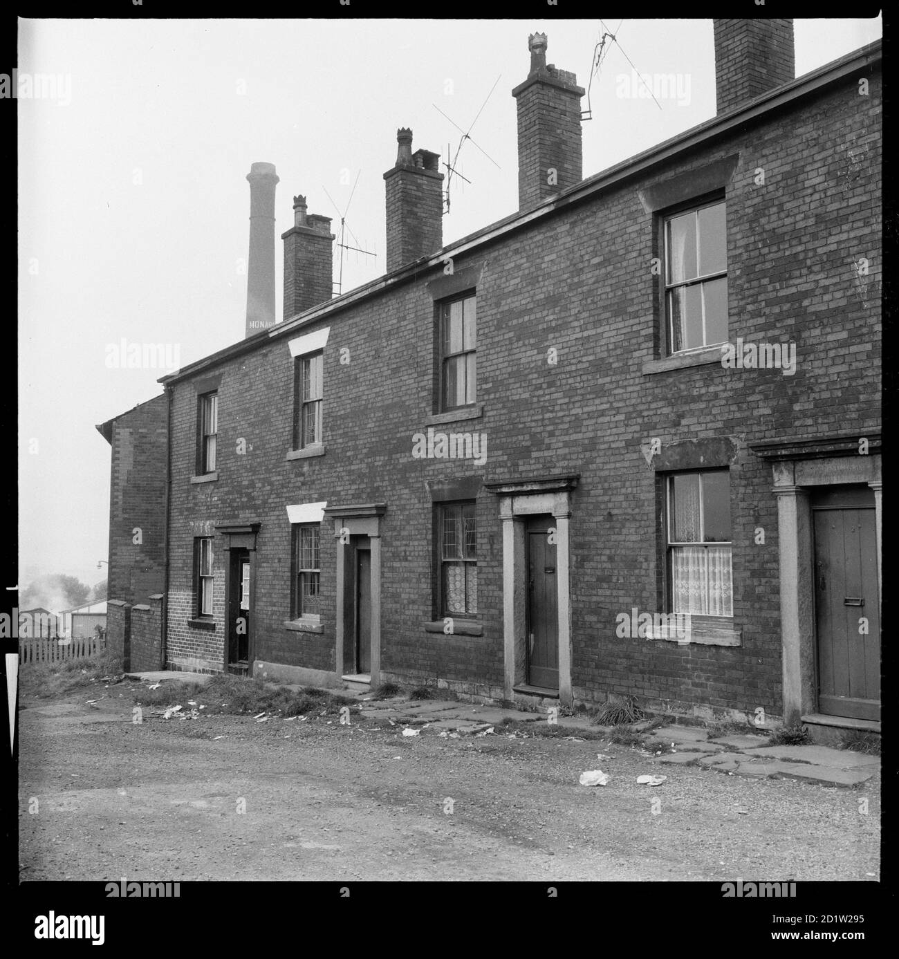 Das Äußere von 2-8 Sparrow Street mit dem Kamin von Monarch Mill in Stocking über den Dächern, Oldham, Greater Manchester, Großbritannien. Stockfoto