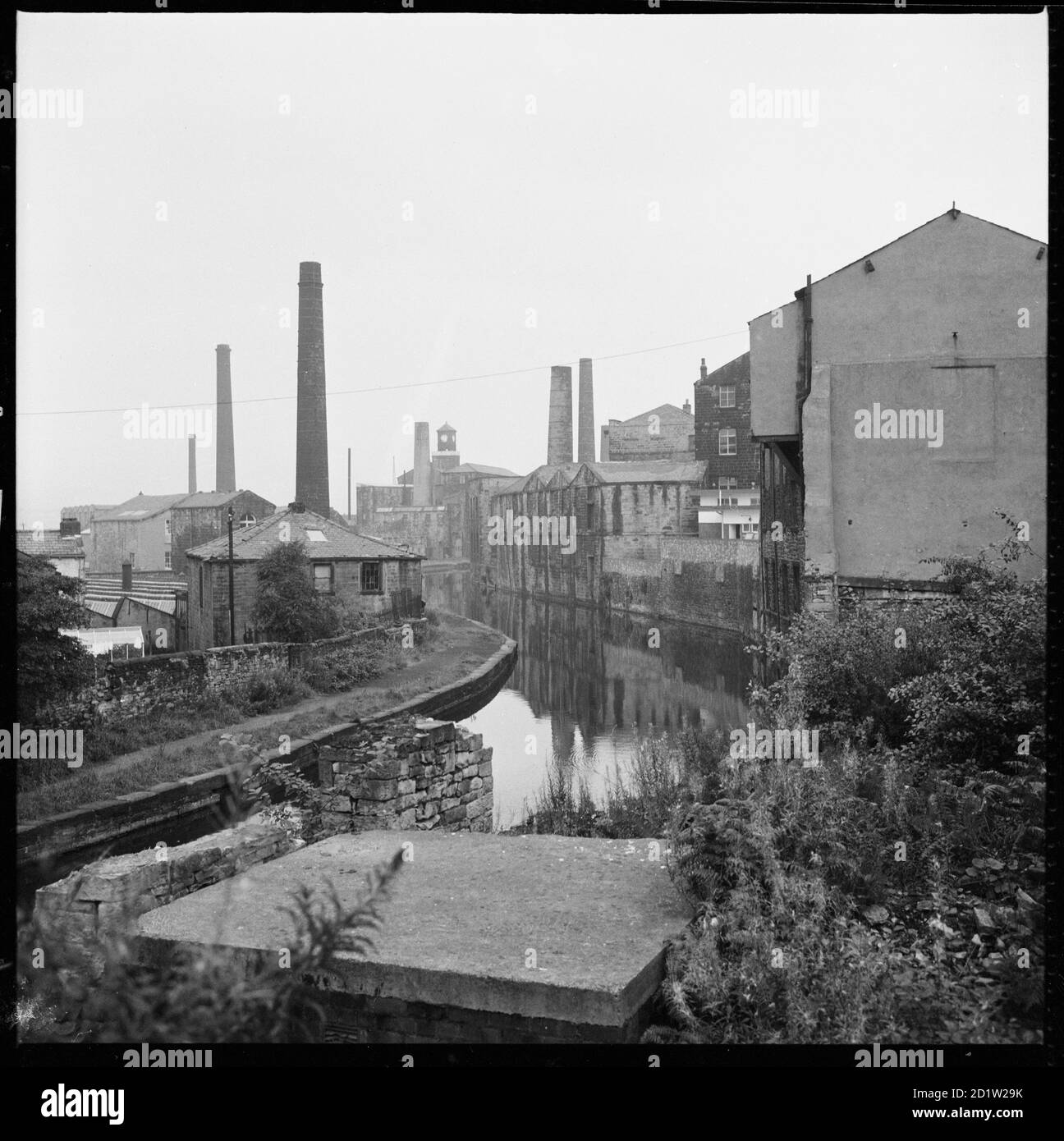 Ein Blick nach Südosten entlang des Leeds und Liverpool Canal von Westgate Bridge zeigt Mühlen und Lagerhallen säumen den Kanal und Clock Tower Mills in der Ferne, Burnley, Lancahire, Großbritannien. Stockfoto