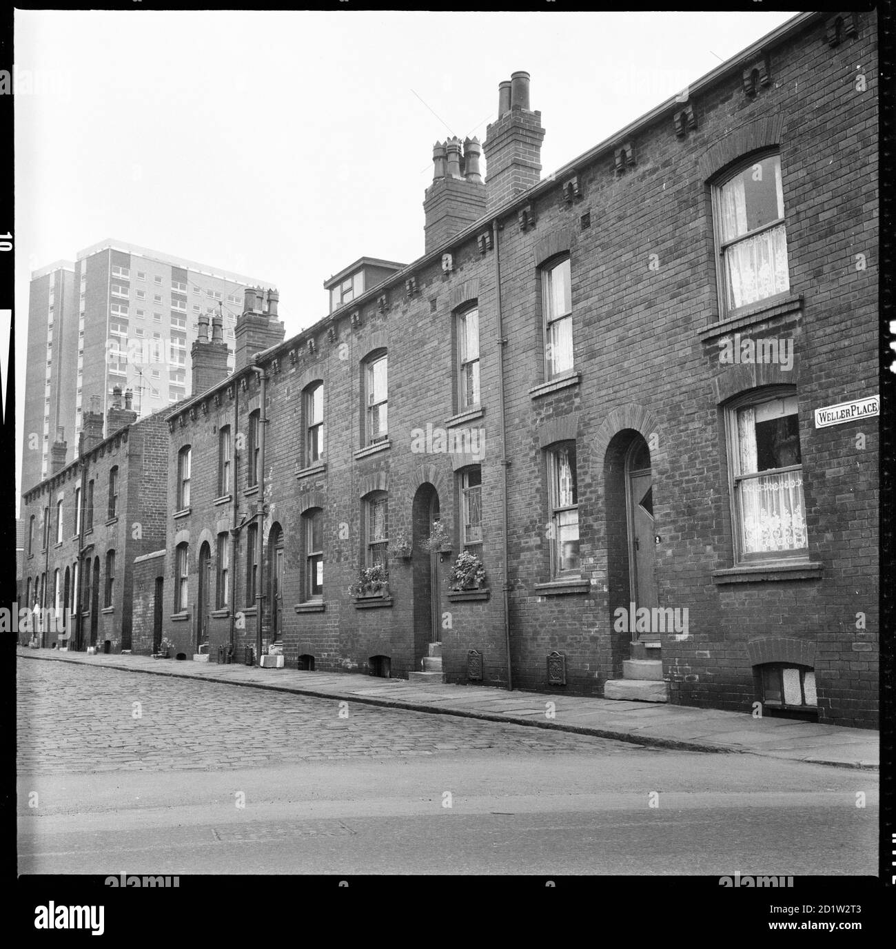 Häuser auf der Südseite des Weller Place mit Nummer 2 im Vordergrund und Scargill Grange Tower Block im Hintergrund, Burmantofts, Leeds, West Yorkshire, UK. Stockfoto