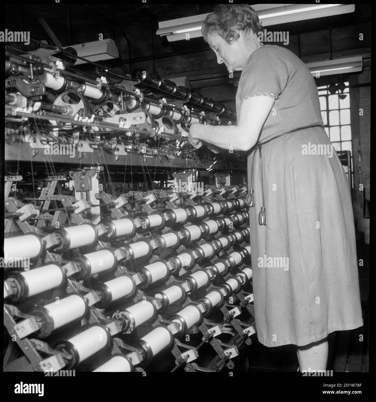 Eine Frau, die eine Garnverdoppelungsmaschine in den Räumlichkeiten von Bentley und Whittles, Seidenherstellern, in Wellington Mills, Strangman Street, Leek, Staffordshire Moorlands, Staffordshire, Großbritannien, betreibt. Stockfoto