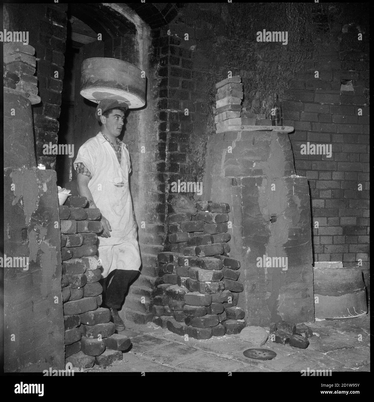 Ein Mann mit einem Saggar auf dem Kopf durch die Wicket-Tür eines Ofens in der Royal Albert Pottery, Teil von Alfred Meakins Royal Albert & Victoria Potteries. Stockfoto