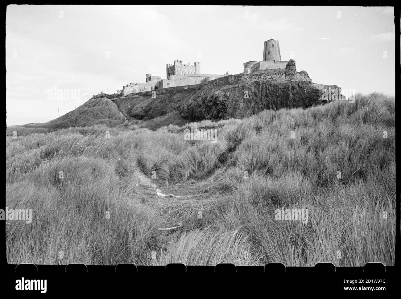 Allgemeine Ansicht von Bamburgh Castle, von Nord-West gesehen und zeigt die äußere Richtung im Vordergrund, mit der Windmühle an der Spitze der Station, und die innere Station im Hintergrund. Stockfoto