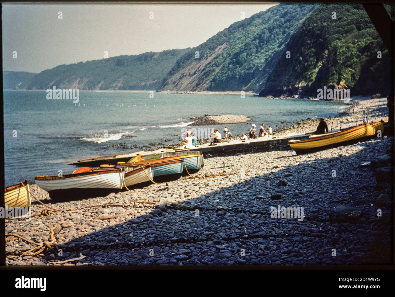 Clovelly Harbour, Clovelly, Torridge, Devon. Ein Blick nach Südosten über das Vorland von Clovelly Harbour, mit kleinen Booten auf dem Kiesel und Menschen sitzen und stehen auf dem Slipway und Strand dahinter. Stockfoto