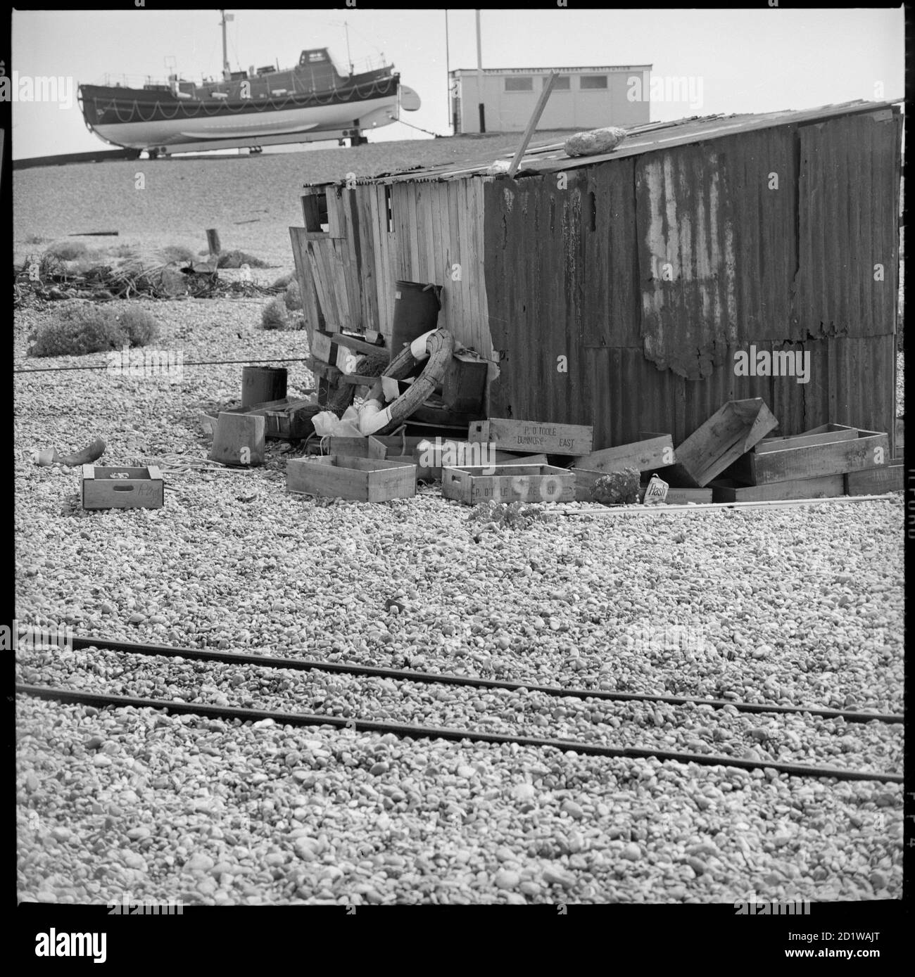 Dungeness, Lydd, Shepway, Kent. Eine Hütte am Strand von Dungeness mit dem RNLI Rettungsboot im Hintergrund. Stockfoto