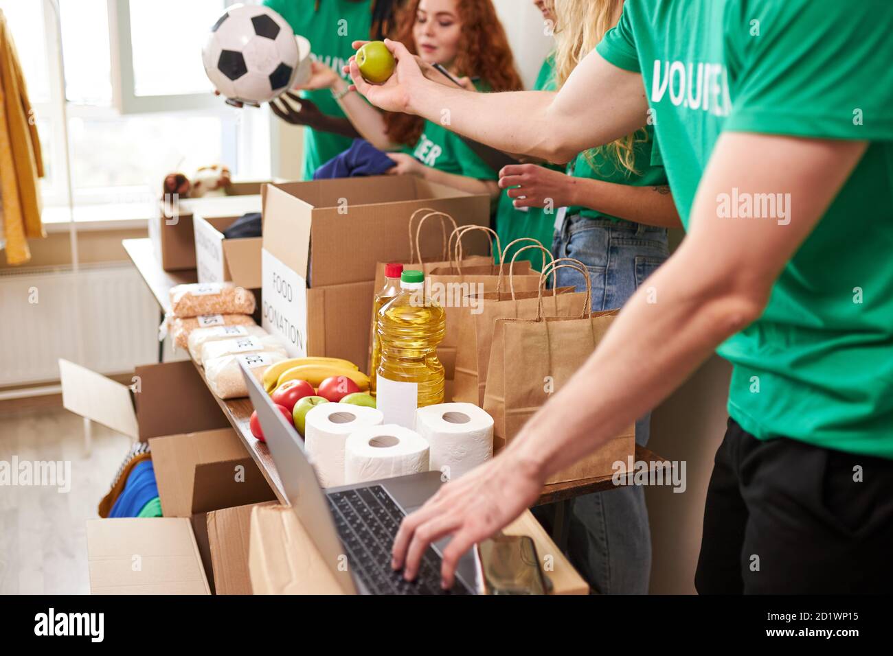 Gruppe von verschiedenen Menschen sortieren durch gespendete Lebensmittel Gegenstände während Freiwilligenarbeit in der Gemeinschaft, verwenden sie Kartons für das Sammeln von Spenden Stockfoto